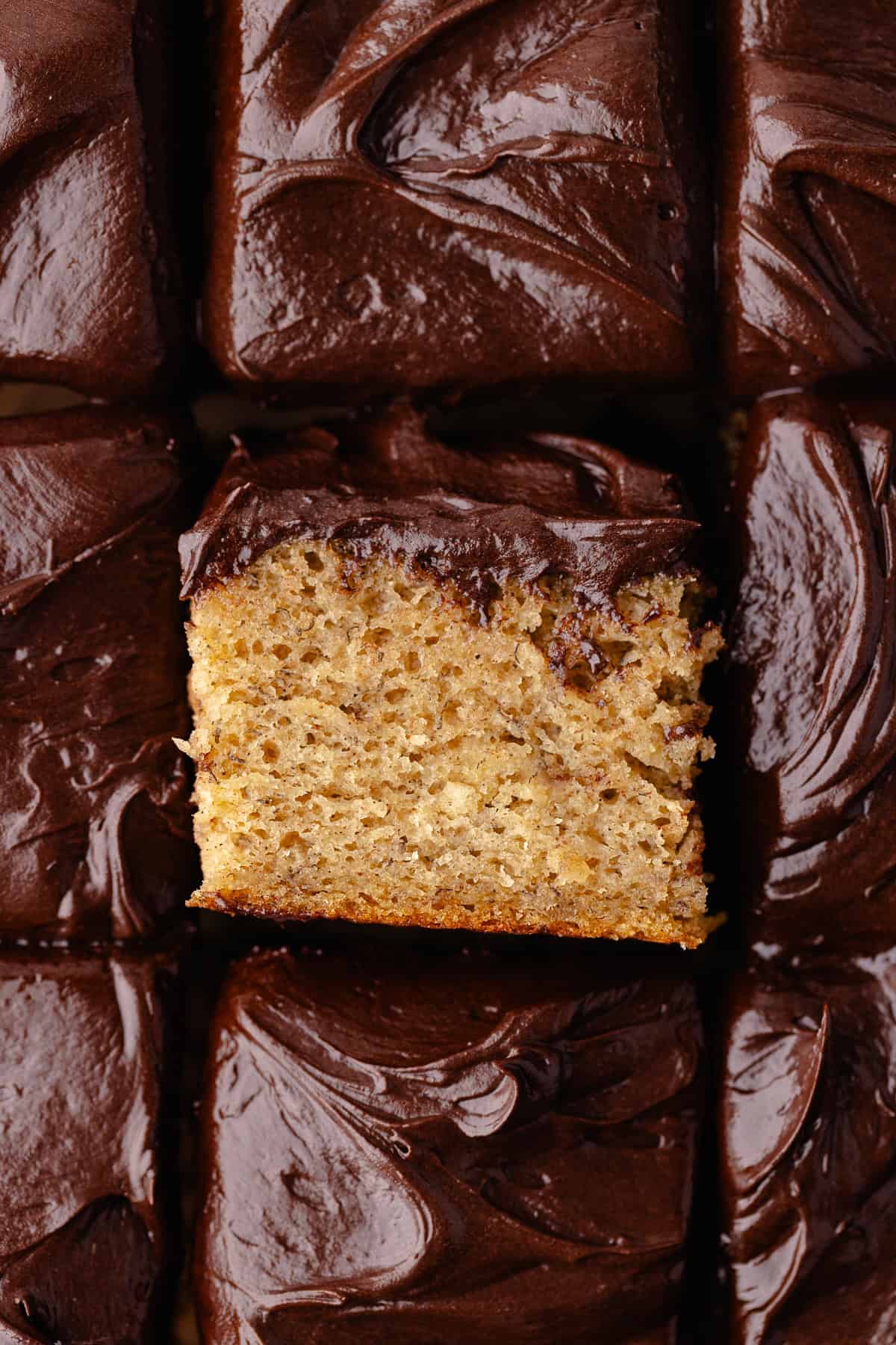 Banana cake with chocolate frosting squares on a wire rack.