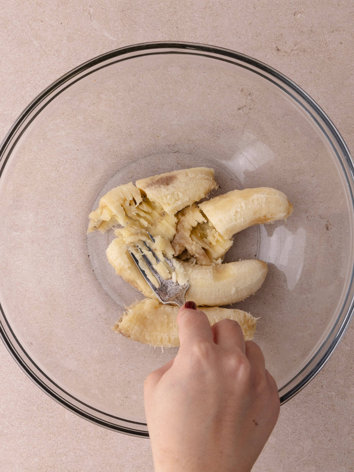 A fork mashed bananas in a large mixing bowl.