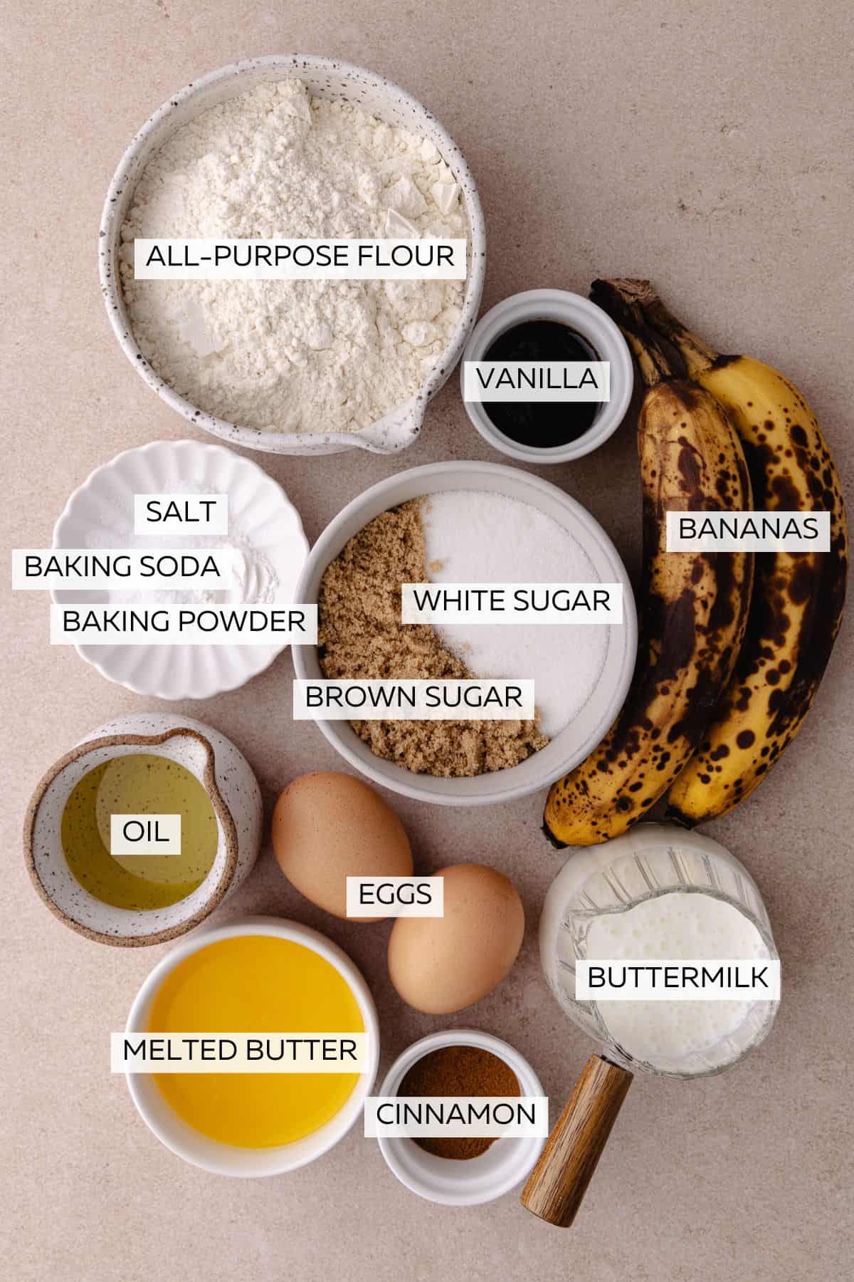 Banana cake ingredients which include, flour, baking powder, baking soda, cinnamon, salt, butter, oil, eggs, brown sugar, white sugar, buttermilk, bananas, vanilla and oil.