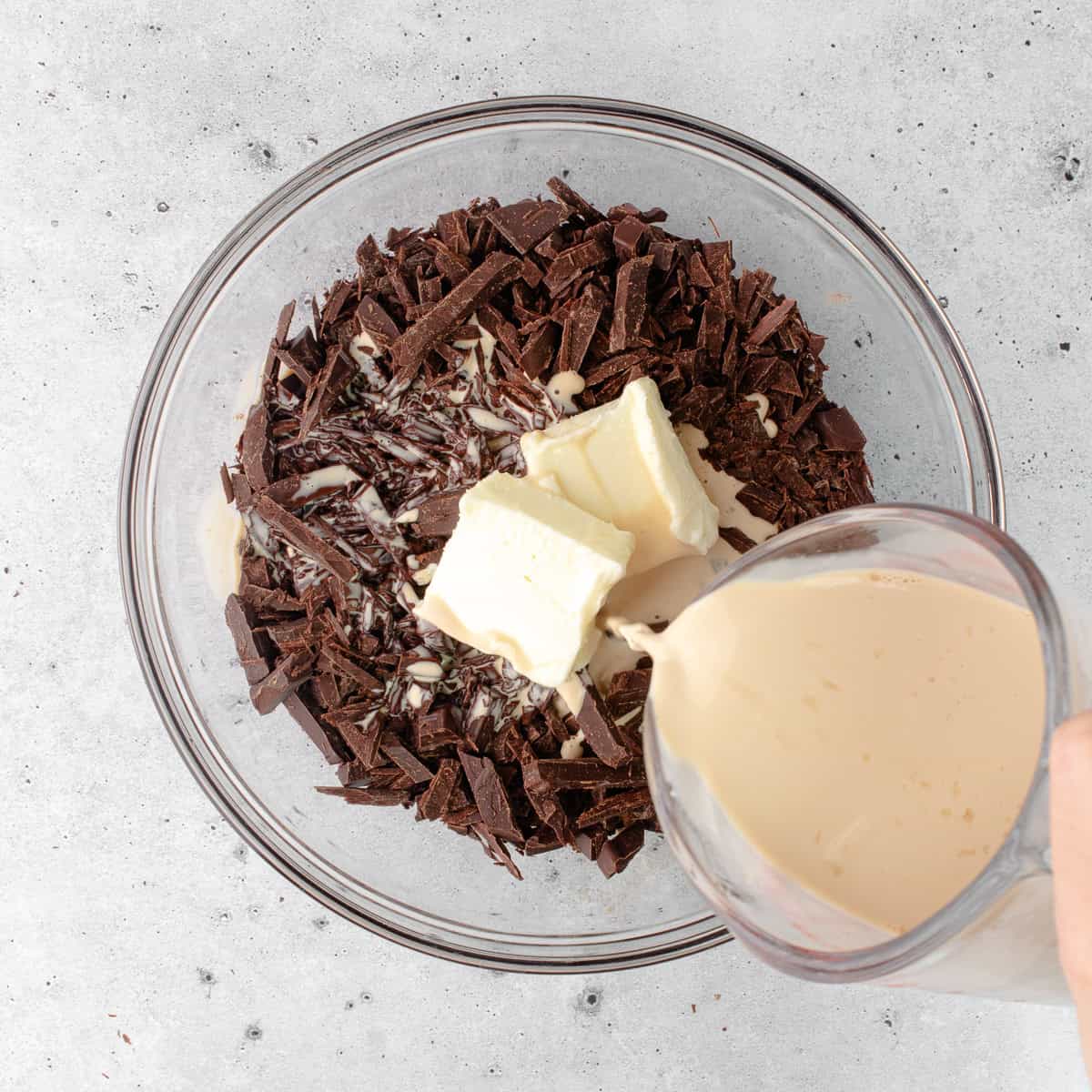 Earl grey infused hot cream is poured over finely chopped chocolate and butter that is sitting in a medium bowl.