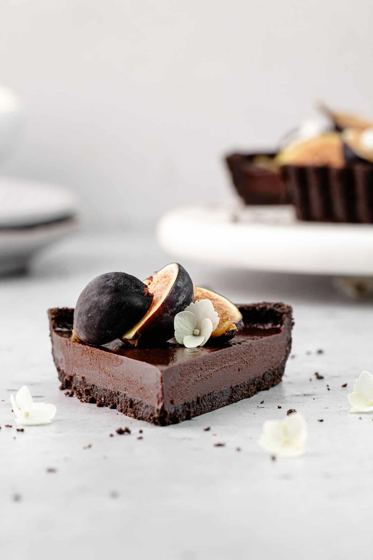 A close up of the straight-on view of a slice of chocolate earl grey tart garnished with fresh figs.