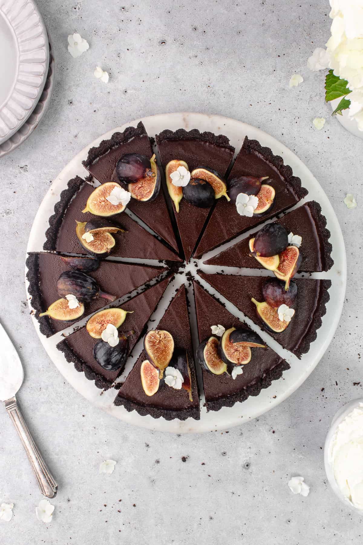 Slices of chocolate earl grey tart garnished with fresh figs and flowers are on a marble serving plate.