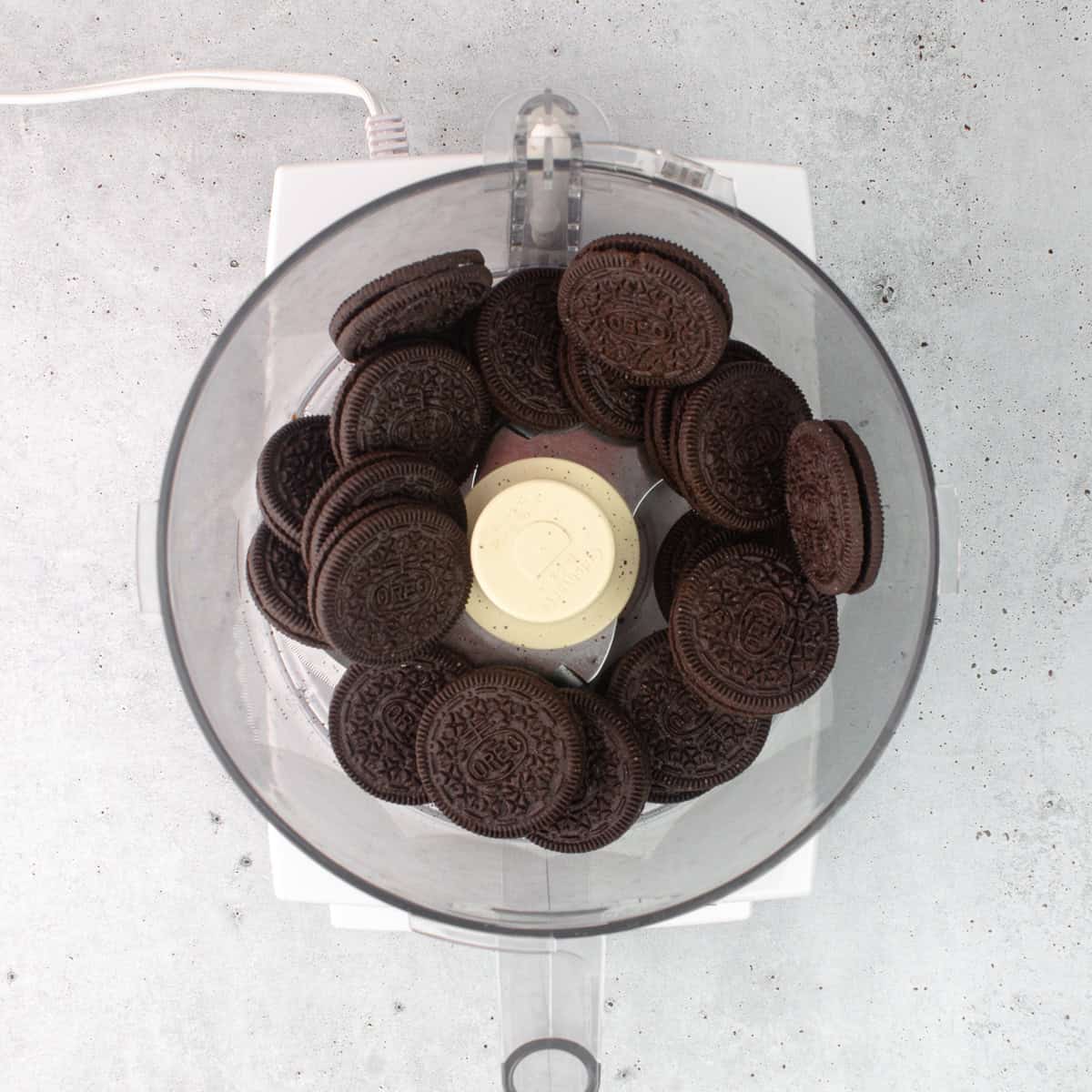 Whole oreo cookies are in the bowl of a food processor.