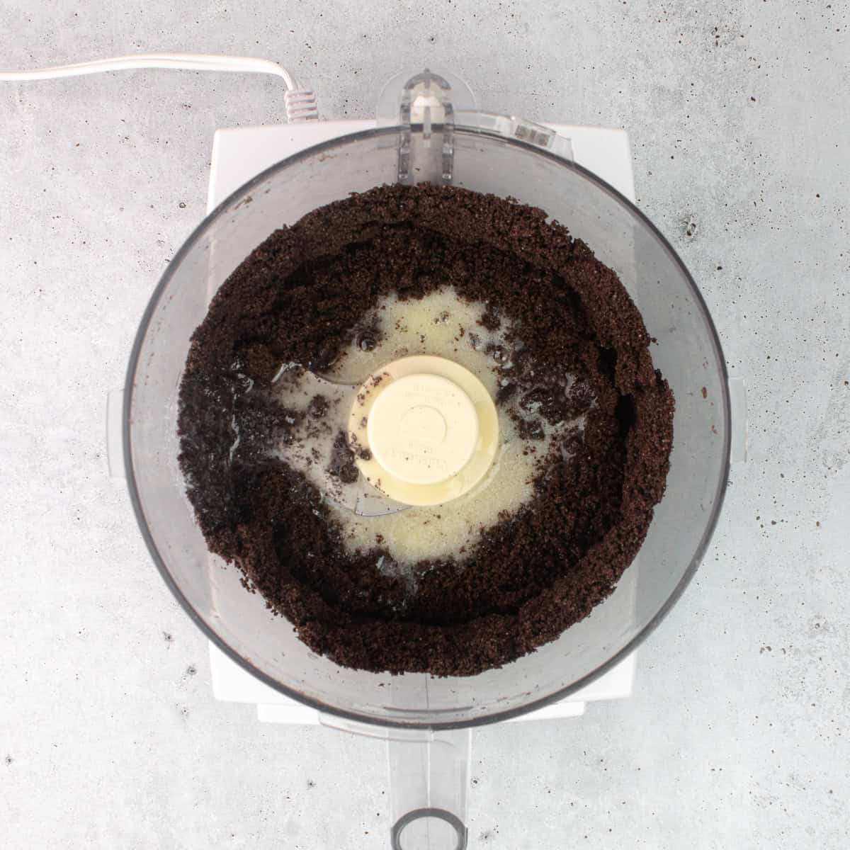 Melted butter is added into the food processor filled with Oreo cookie crumbs.