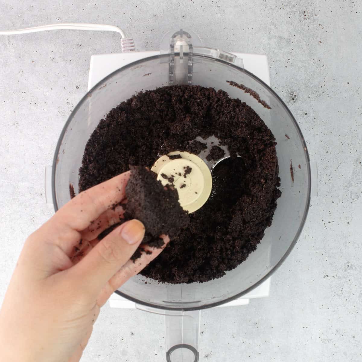 Oreo cookie crumbs are pressed together over a food processor.