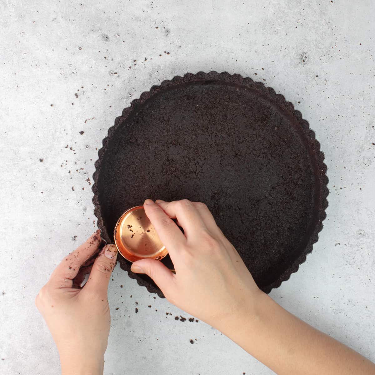 Oreo cookie crumbs are pressed in a round tart pan.