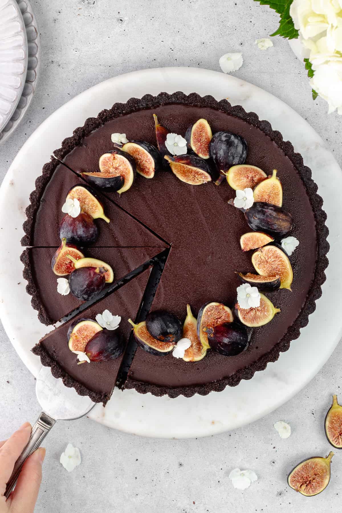 Slices of chocolate earl grey tart garnished with fresh figs and flowers are on a marble serving plate.