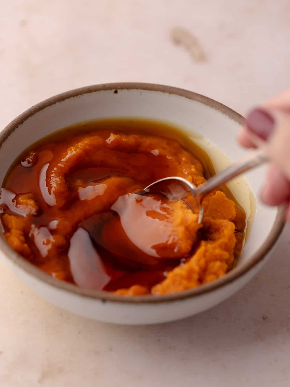 Pumpkin puree and maple syrup are stirred together in a small bowl.