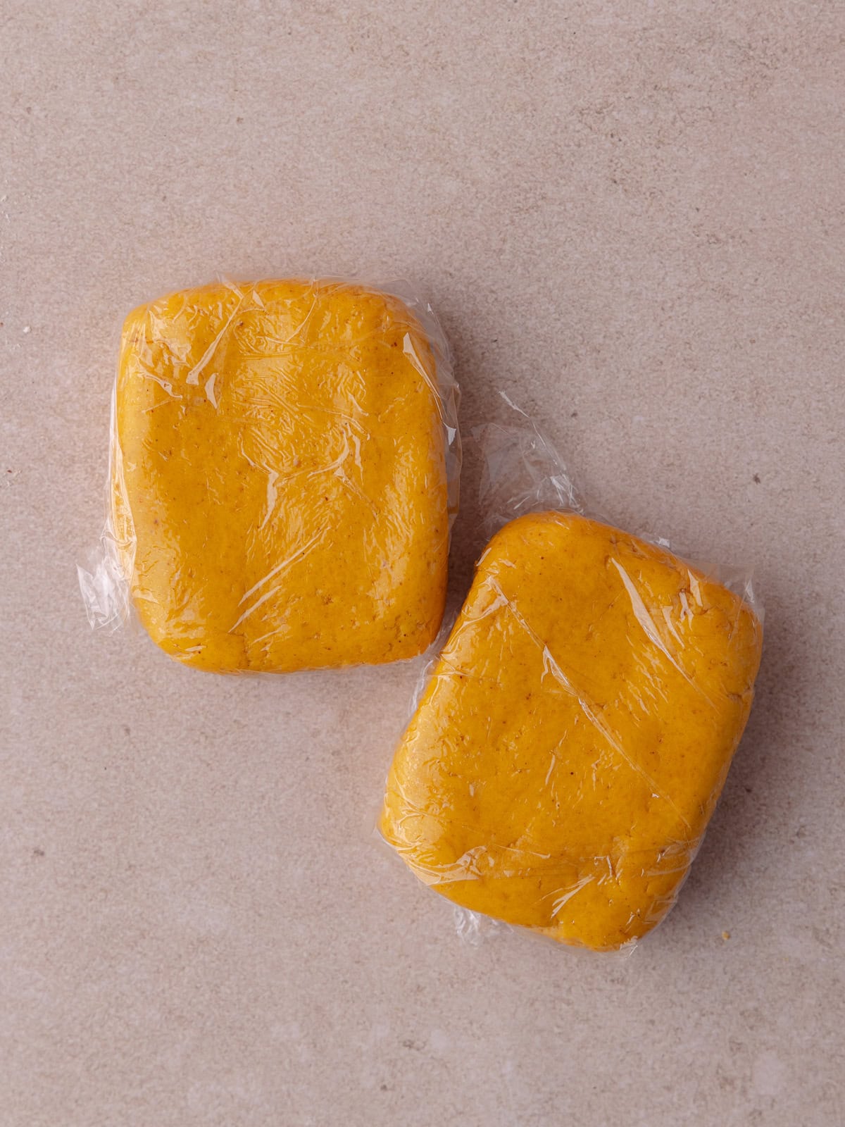 The pumpkin cheddar dough is divided into two pieces and are individually wrapped in plastic wrap and placed in the fridge.