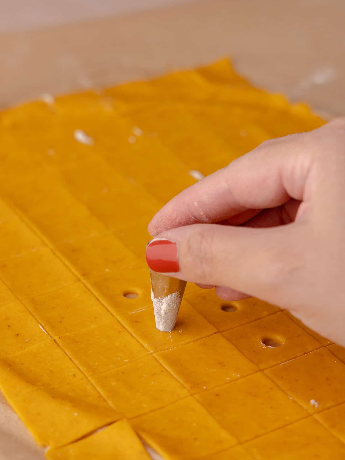 A hole is punched out in each small square of cracker dough.