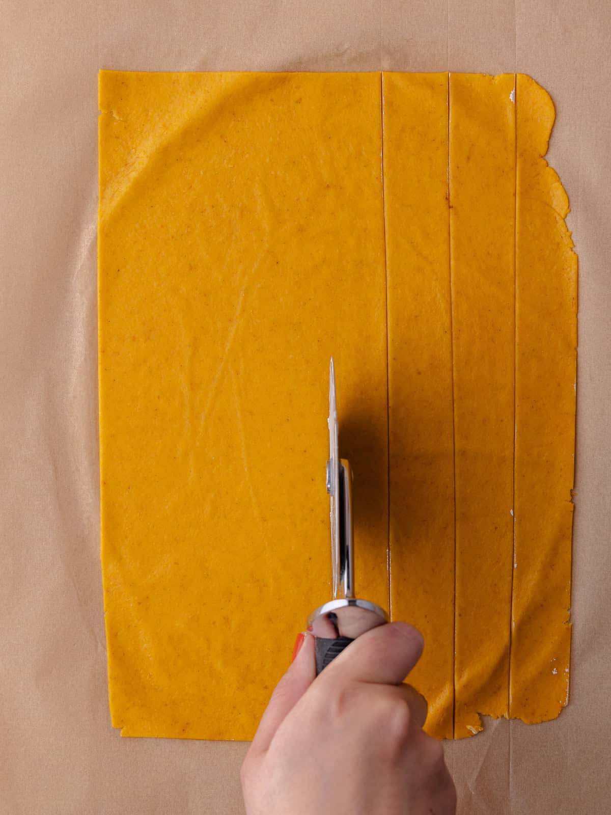 A hand uses a pizza cutter to cut the rolled out pumpkin cheddar cracker dough into small 1 inch squares.