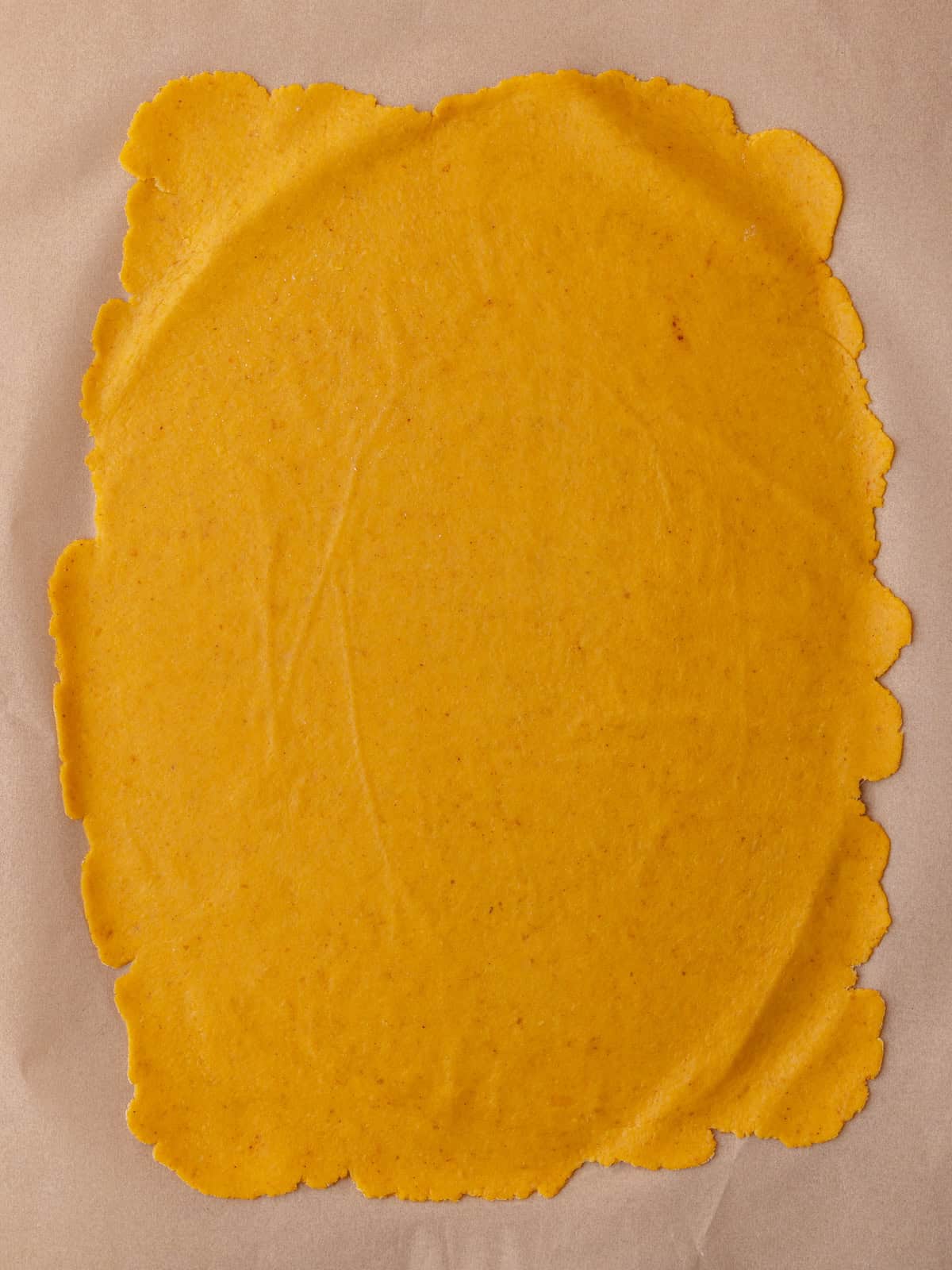 The pumpkin cheddar cracker dough is rolled out extremely thin on top of a piece of parchment paper.