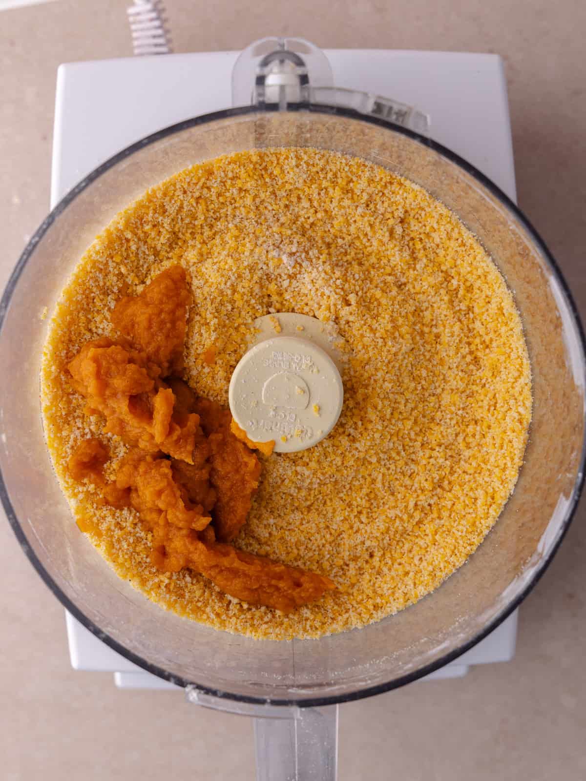 Pumpkin puree is added to the all purpose flour, cornstarch, cheddar cheese, butter and paprika mixture in the bowl of a food processor.