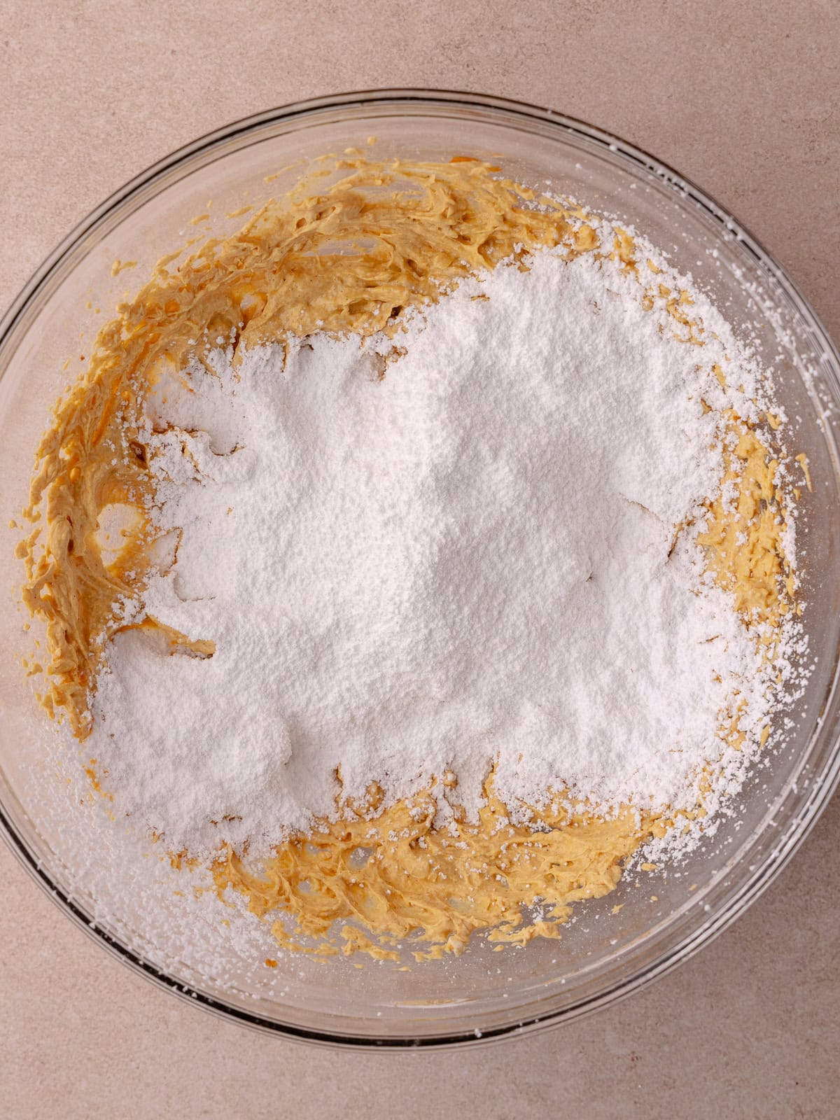 Sifted powdered sugar is added to the pumpkin cheesecake mixture.