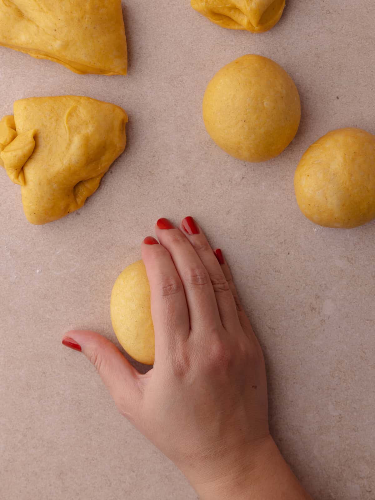 A hand forms a claw shape and is placed over the ball of dough. The hand moves in a circular motion until a smooth ball of dough forms.