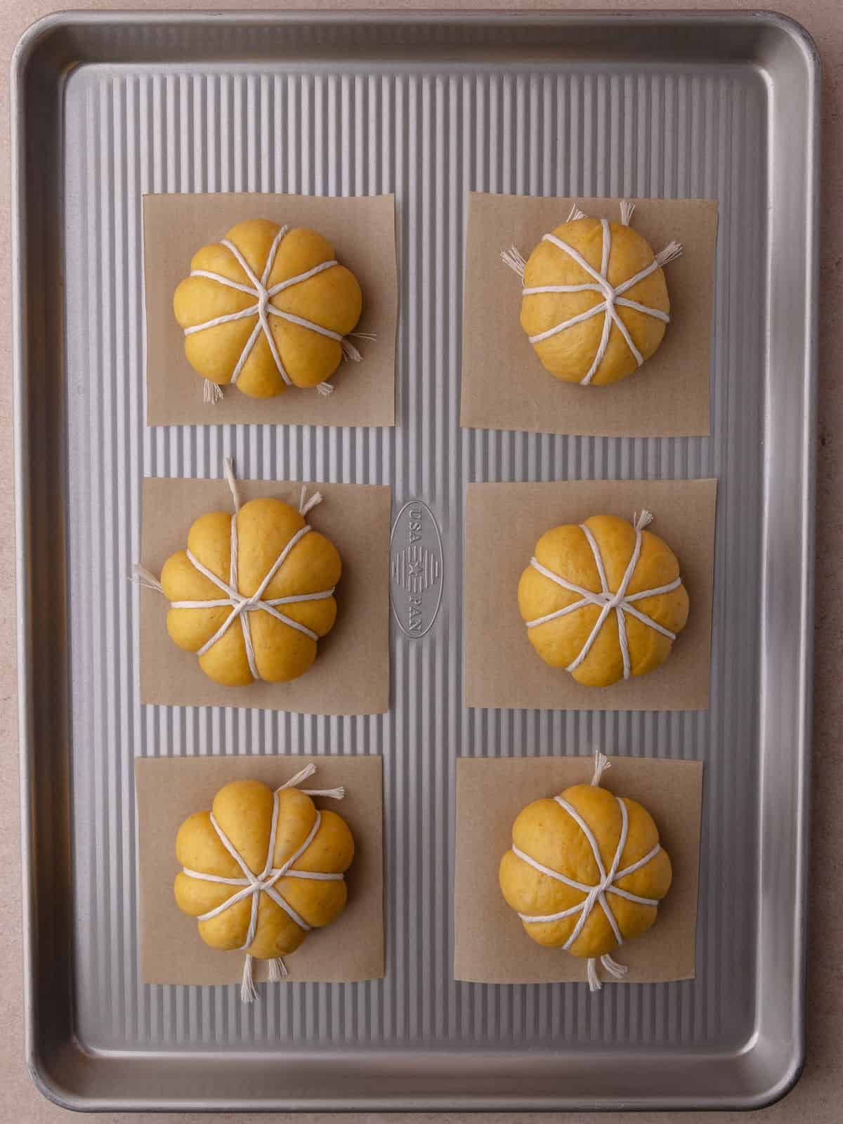 Shaped pumpkin donuts are on top of parchment paper and on a large baking sheet. Donuts will need to proof for about 40 minutes.