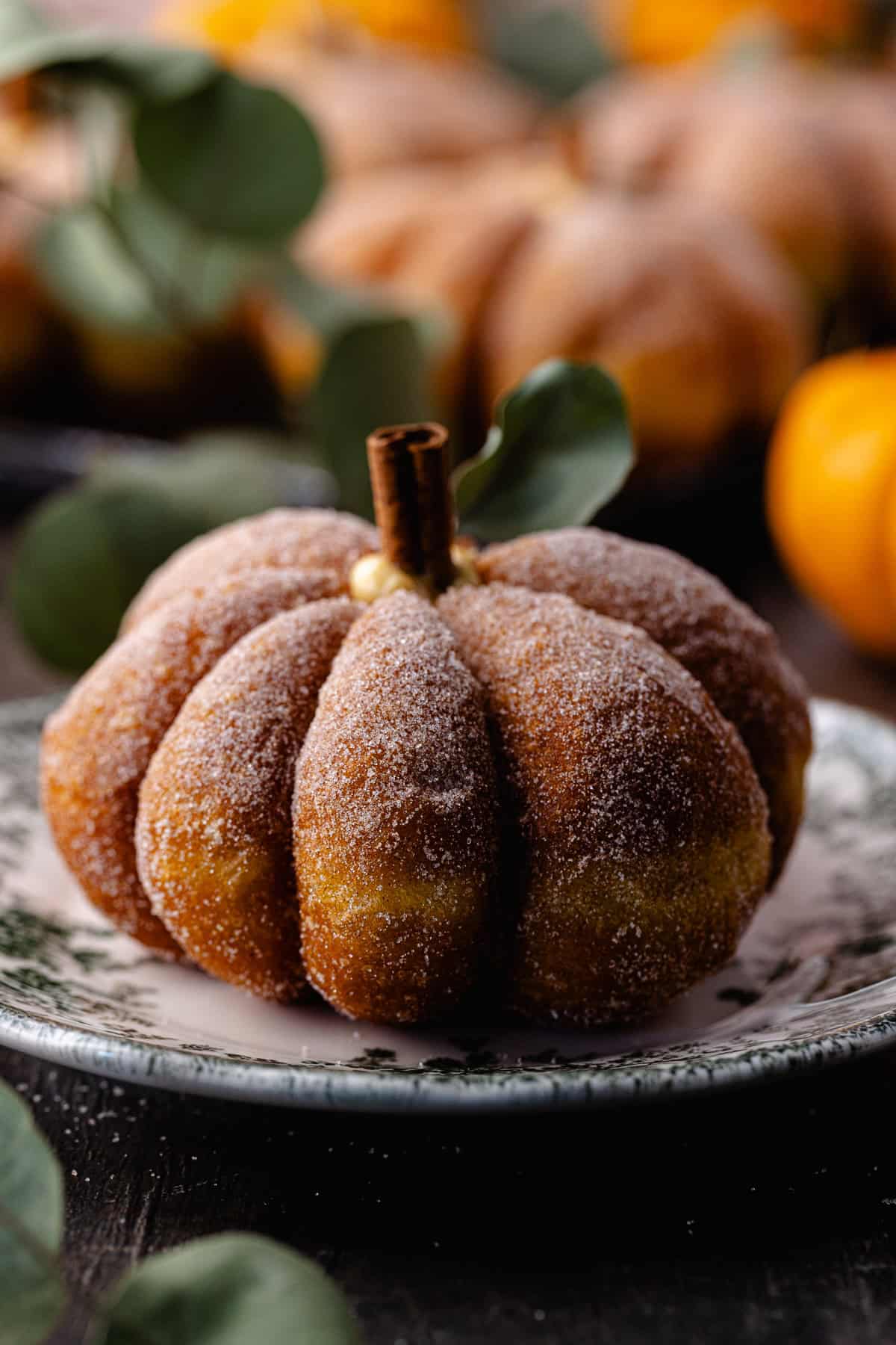 A coated and filled pumpkin shaped donut is sitting on a small dessert plate.