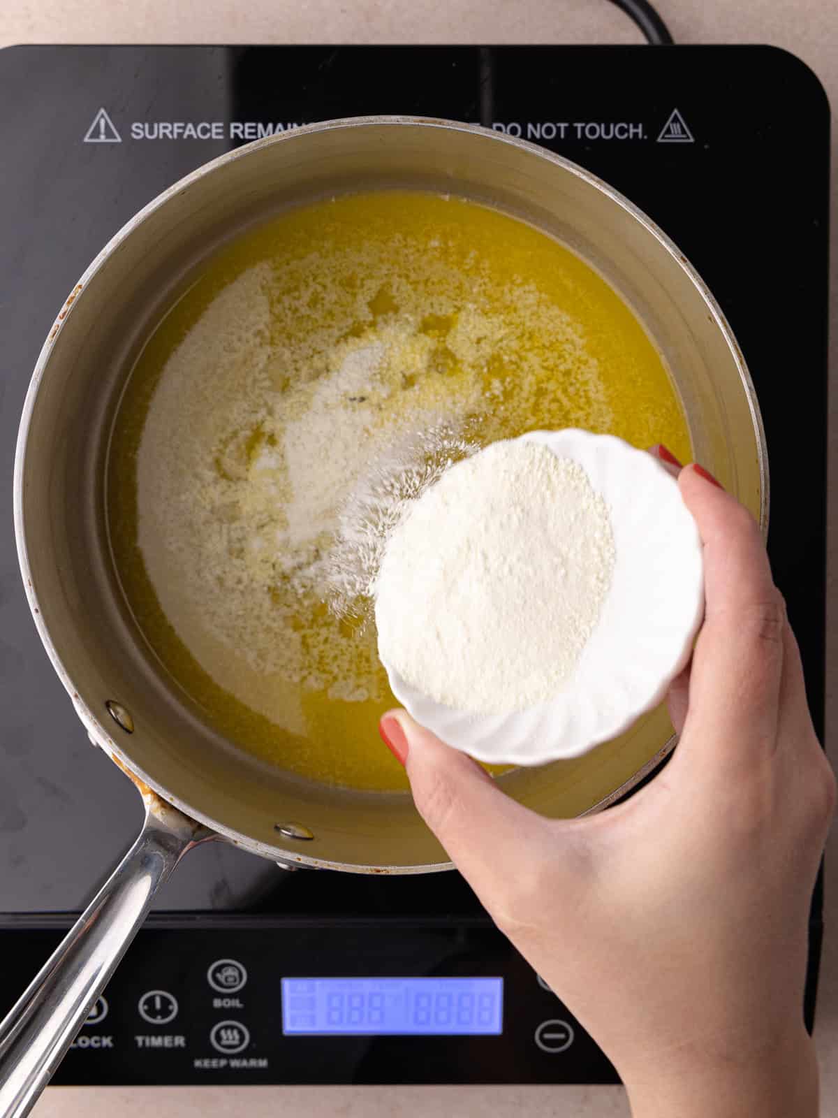 Dry milk powder is sprinkled into a pot of melted butter.