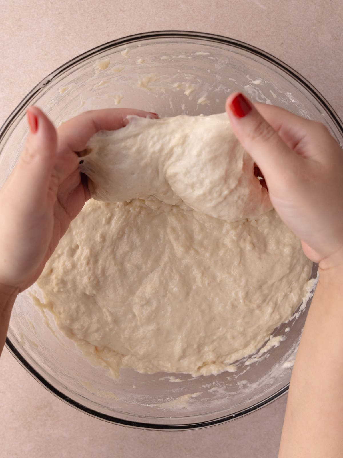 Two hands picks up a side of the dough and is stretched upwards.