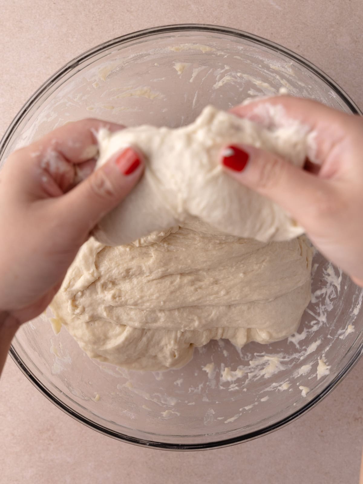 Two hands picks up a side of the dough and is stretched upwards.