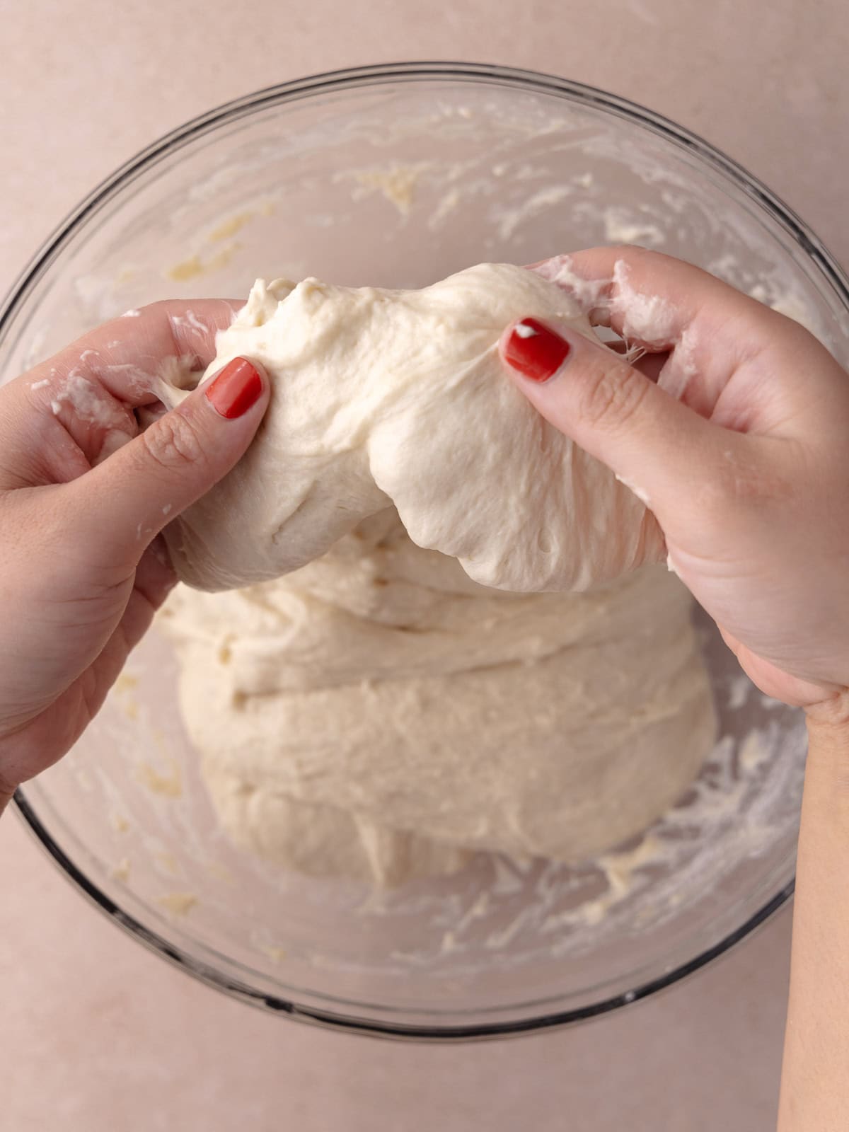 Two hands picks up a side of the dough and is stretched upwards.