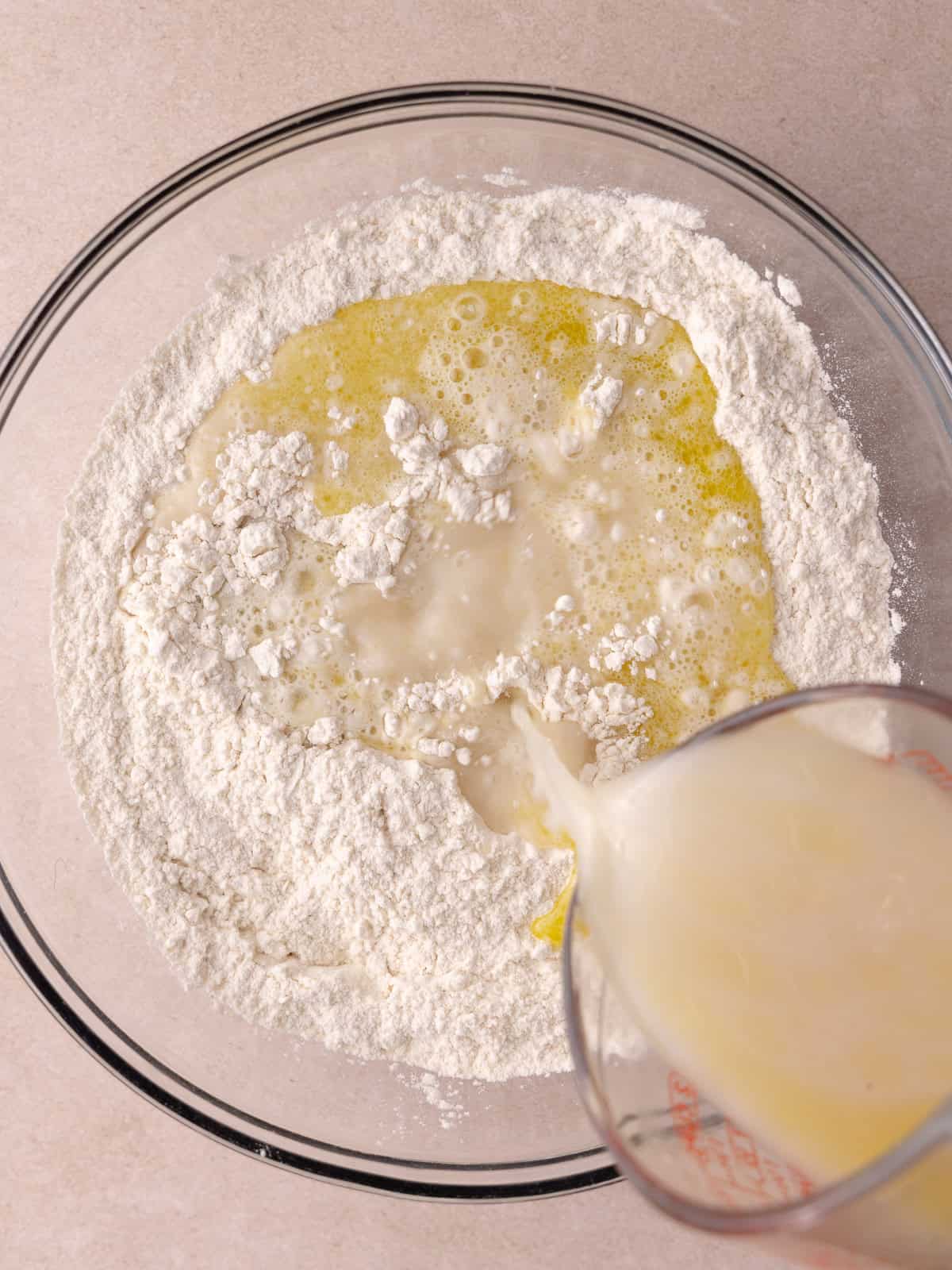 The yeast water mixture is poured into a large bowl that contains bread flour and salt.