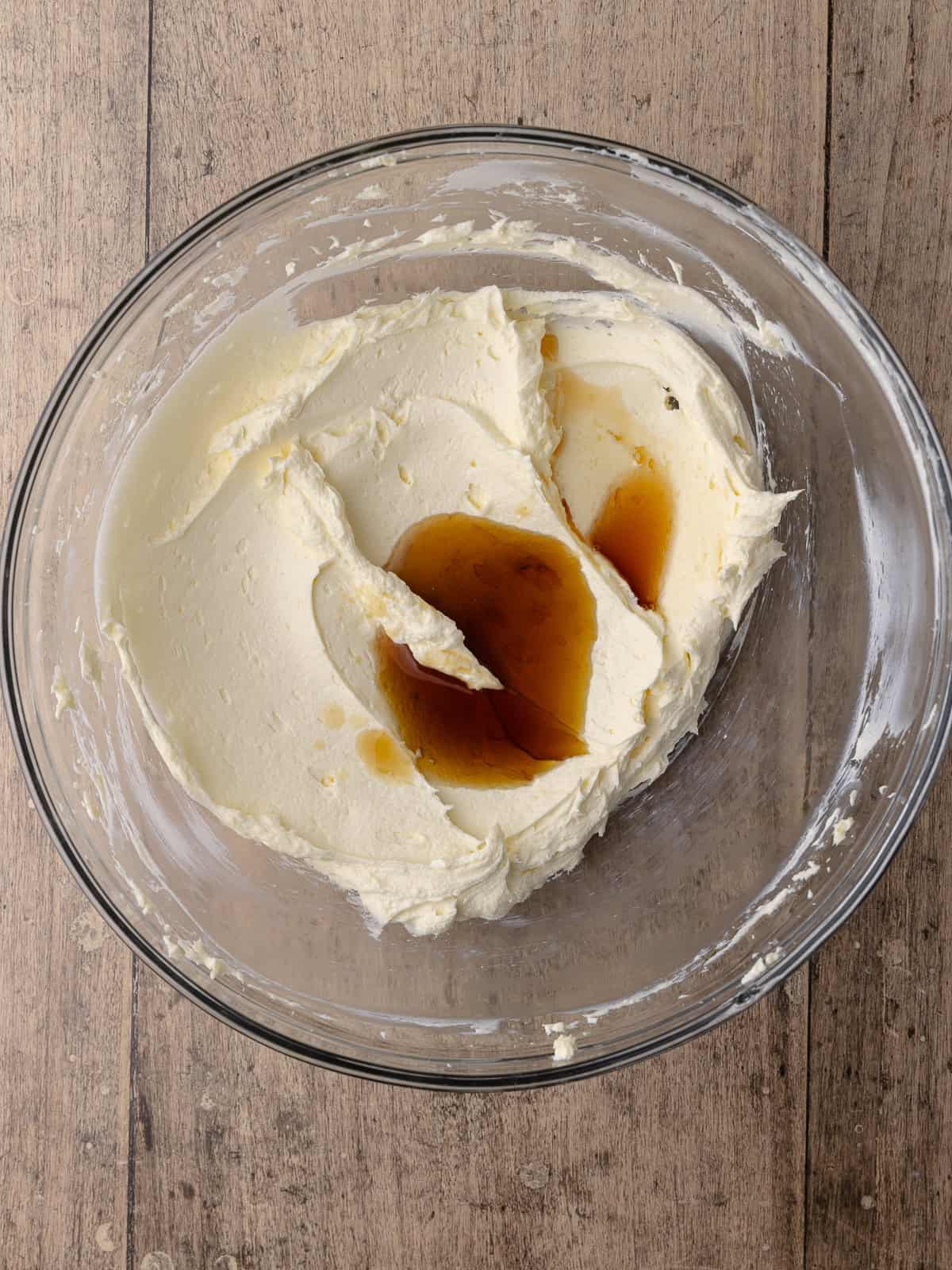 Maple syrup and maple extract is added to a bowl with butter and cream cheese.