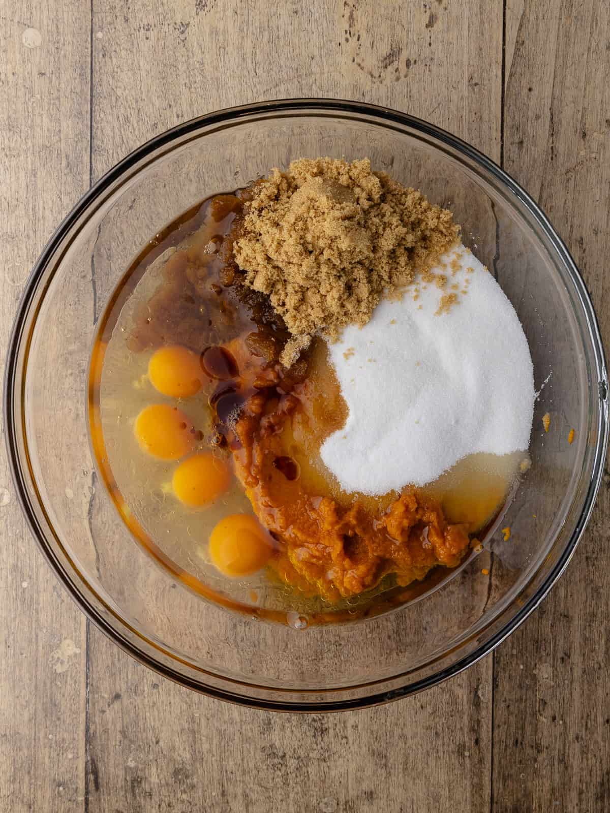 Oil, brown sugar, white sugar, pure pumpkin, 4 eggs and vanilla are in a large glass mixing bowl.