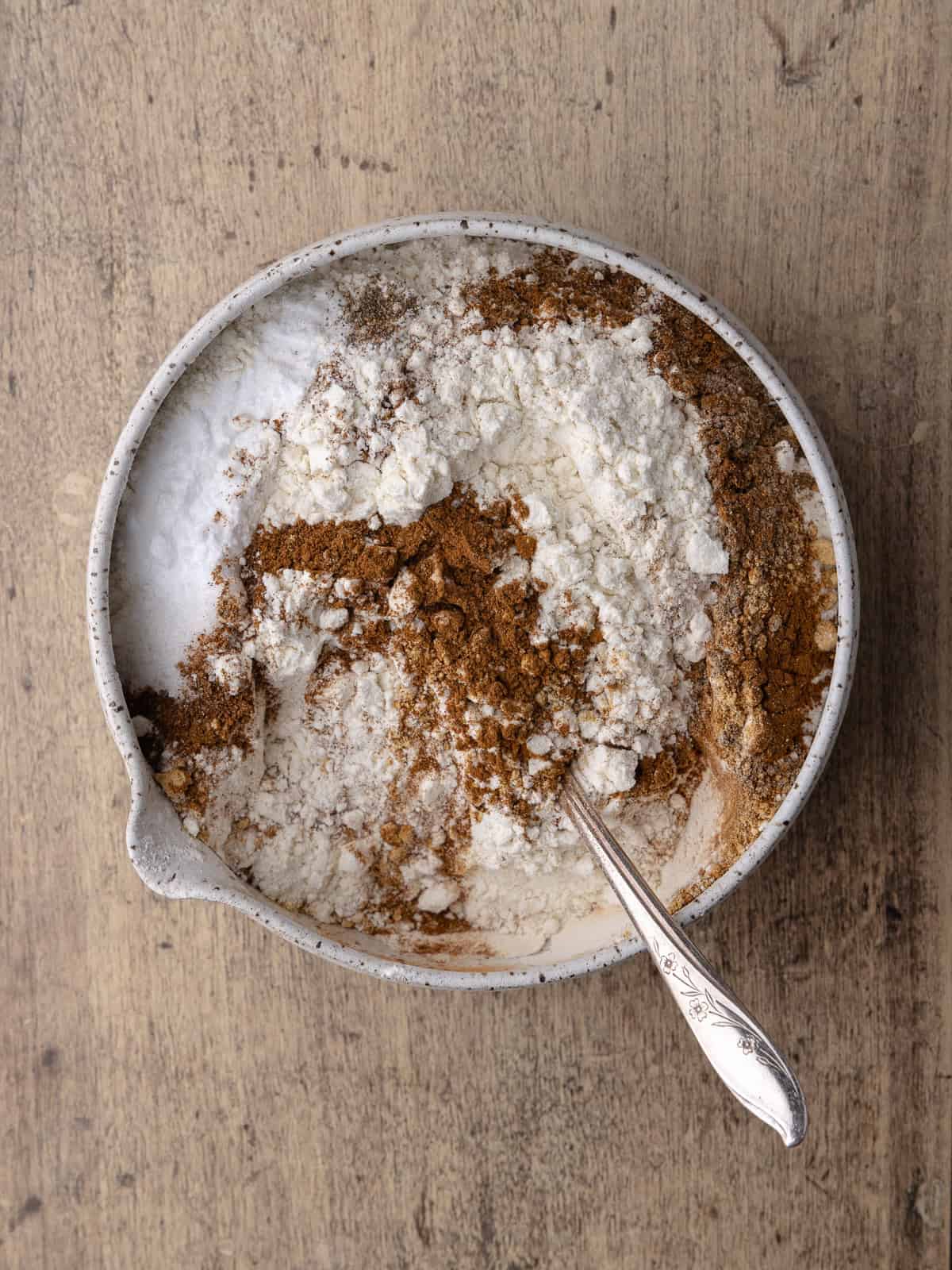 Flour, baking soda, salt, cinnamon, clove, nutmeg, cardamom, ginger and black pepper is in a small mixing bowl.