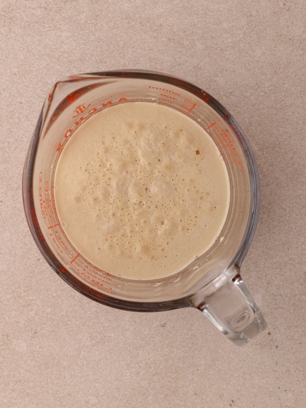 The yeast is bloomed and frothy sitting in a measuring cup.