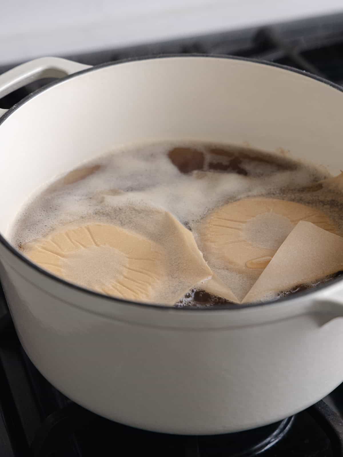 Two bagels are boiling in a large pot of water and barley malt syrup.