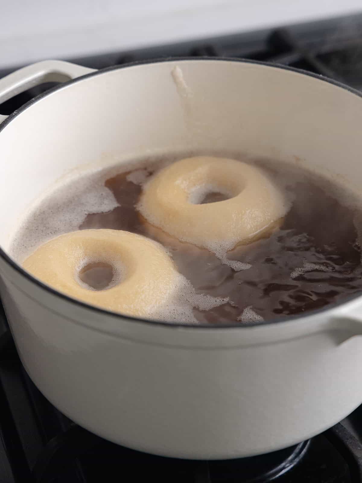 Two bagels are boiling in a large pot of water and barley malt syrup.