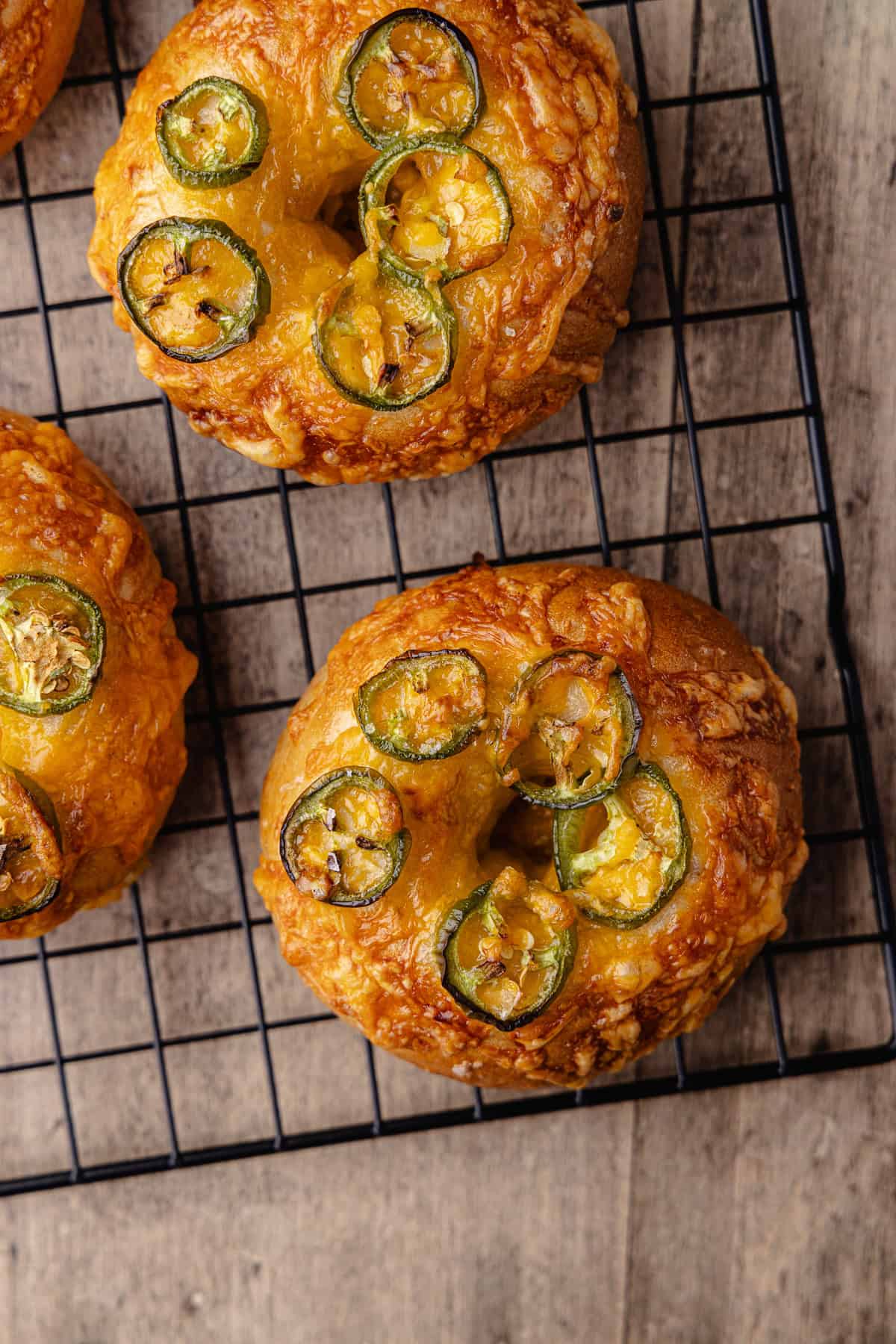 Jalapeño cheddar bagels sitting on a wire rack.