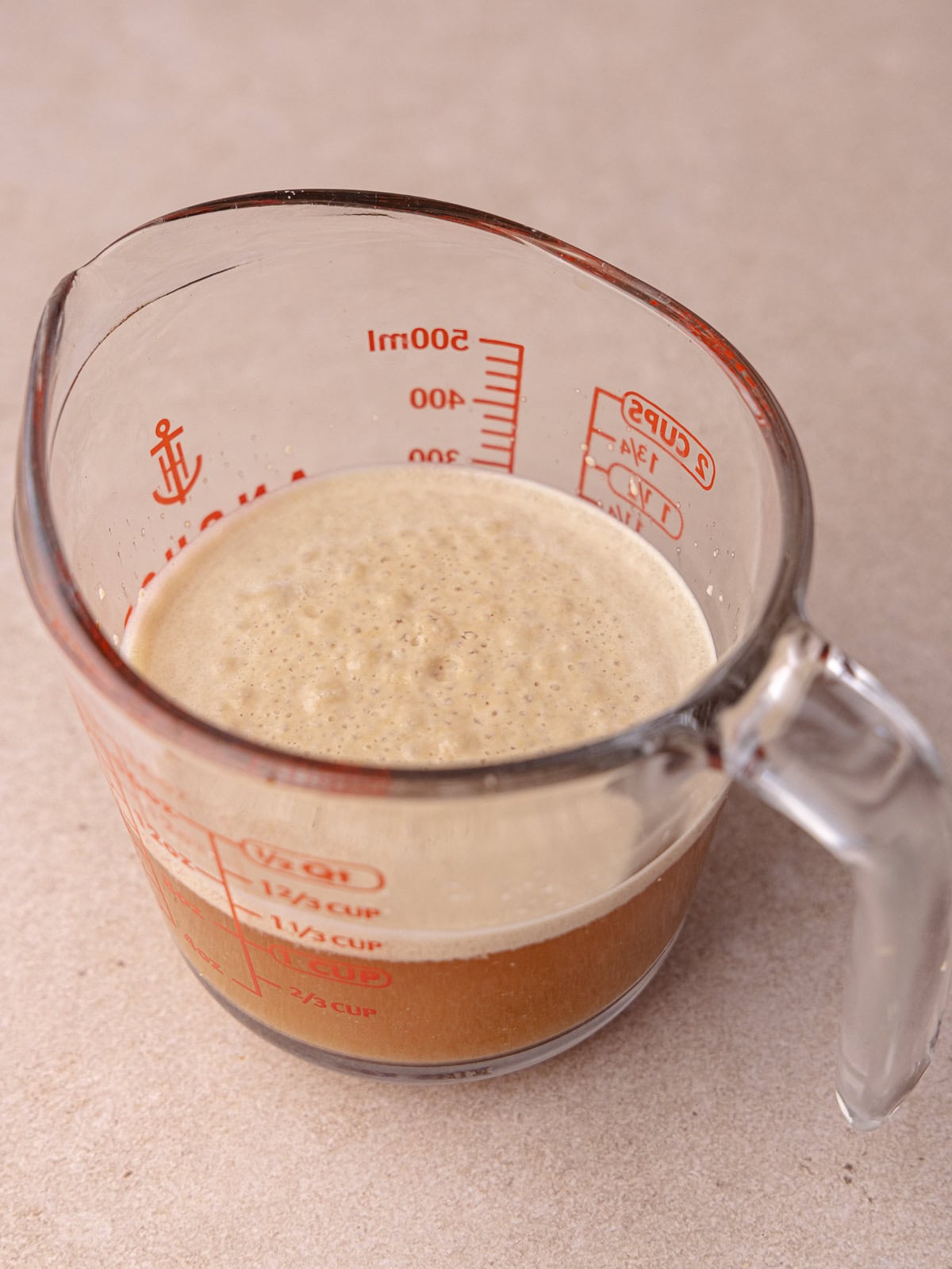 The yeast is bloomed and frothy sitting in a measuring cup.