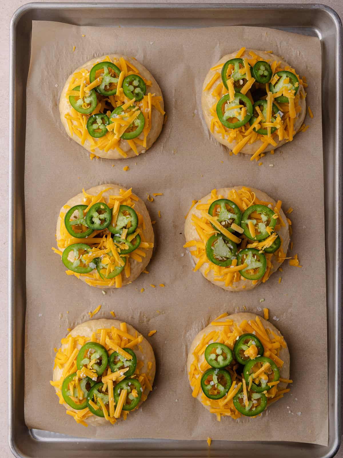 Boiled bagels are topped with shredded cheddar cheese, sliced fresh jalapenos and flaky sea salt.