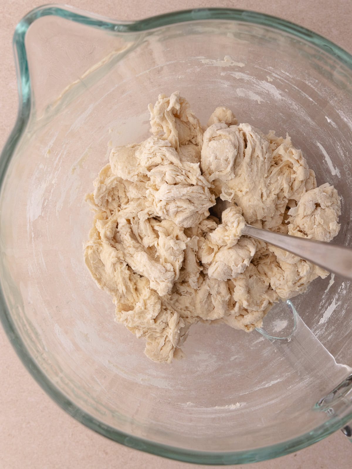 A spoon stirs the bagel dough mixture together and a shaggy ball of dough is formed.