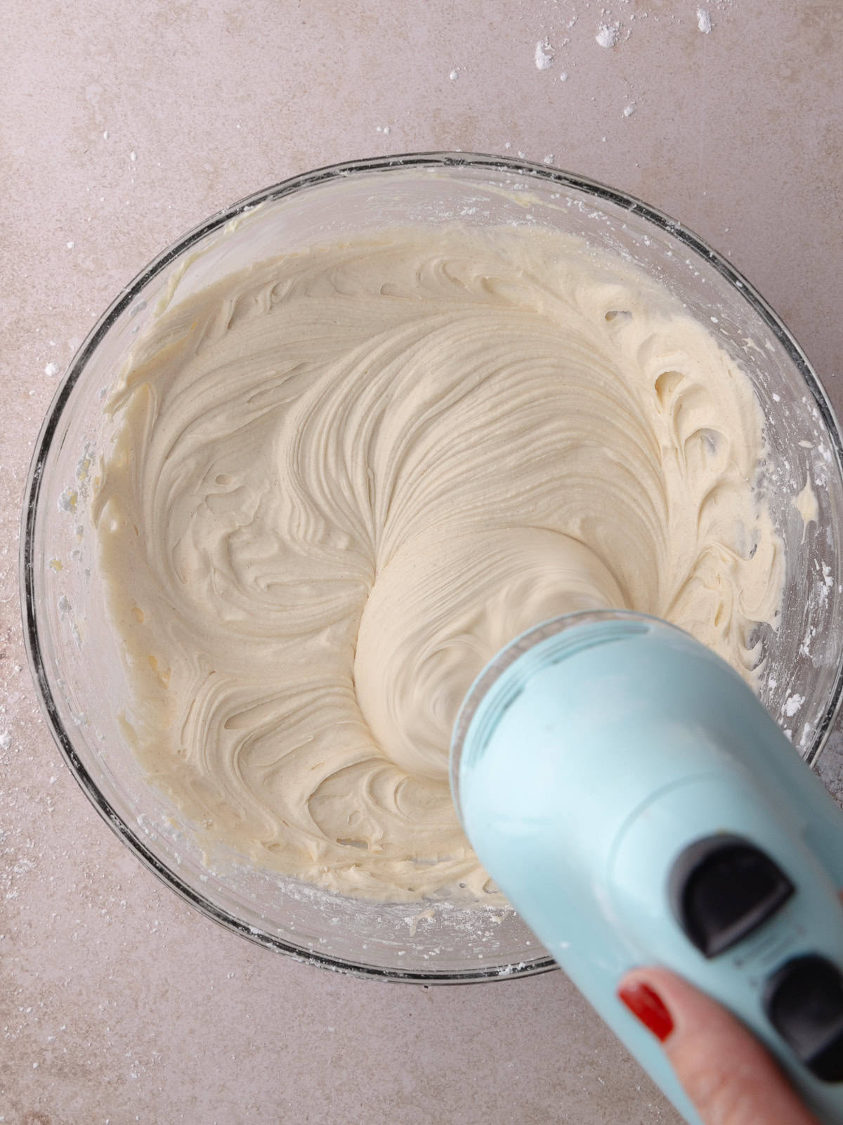 Hand mixer whips maple cream cheese frosting in a large mixing bowl.