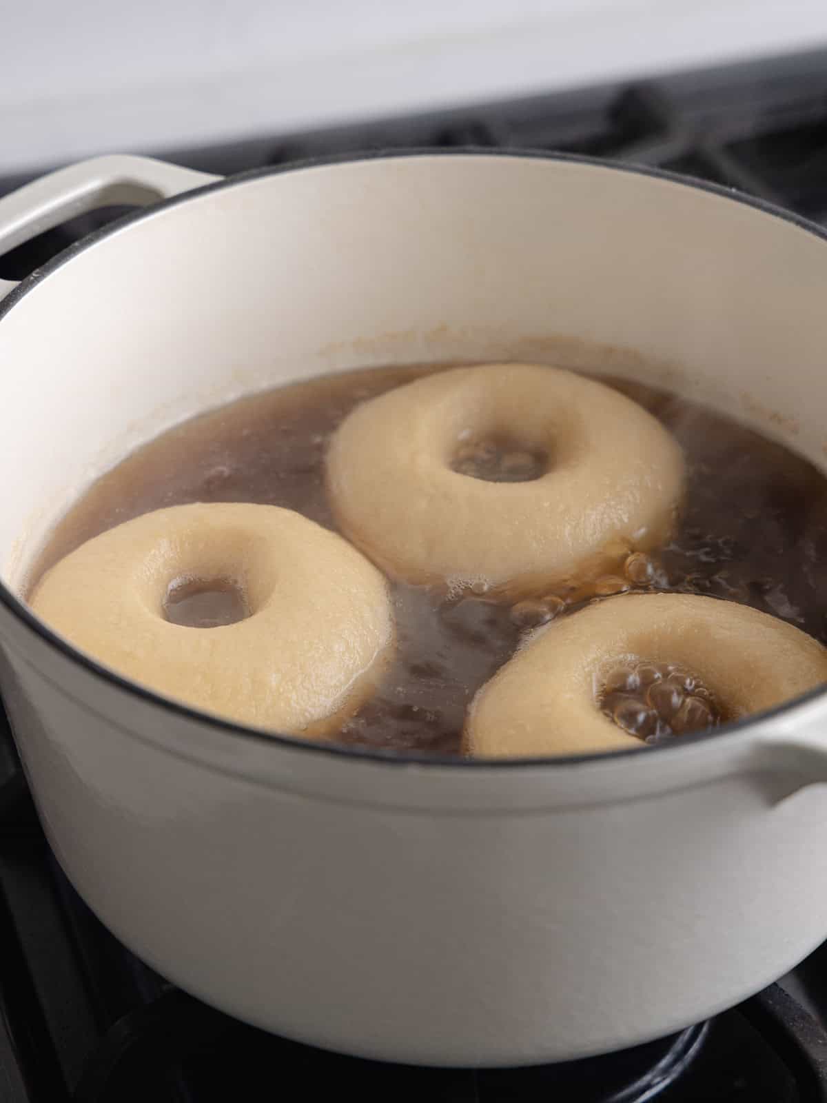 Three bagels are boiling in a large pot of water and barley malt syrup.