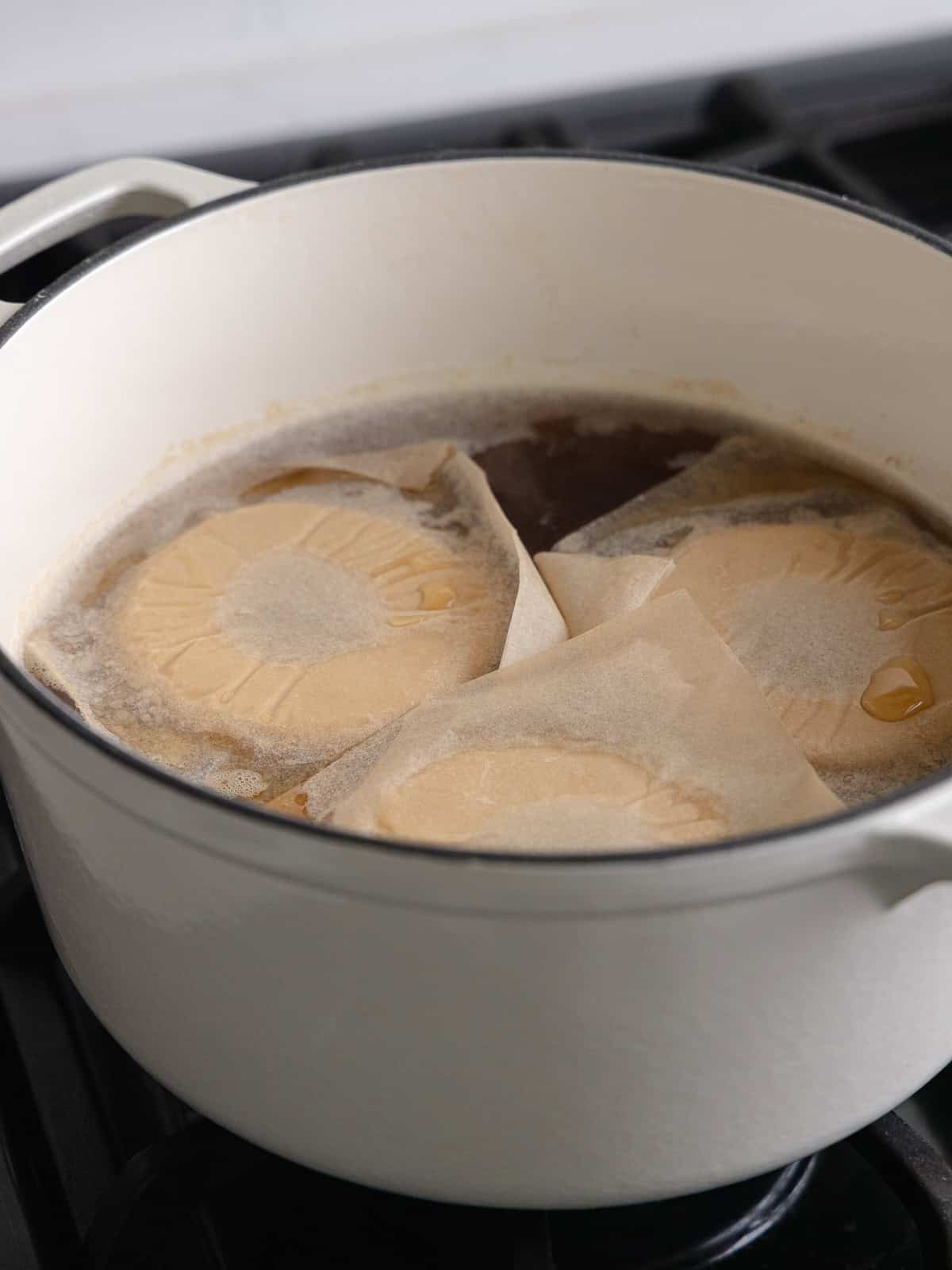 Three bagels are boiling in a large pot of water and barley malt syrup.