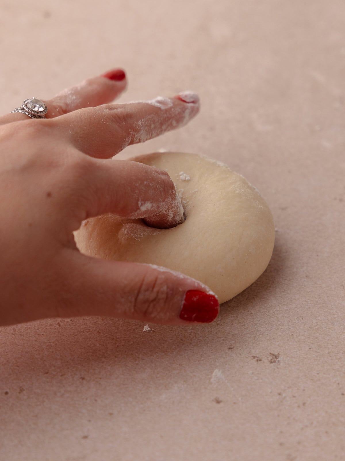 A finger creates a whole in the center of the dough ball to shape the bagels.