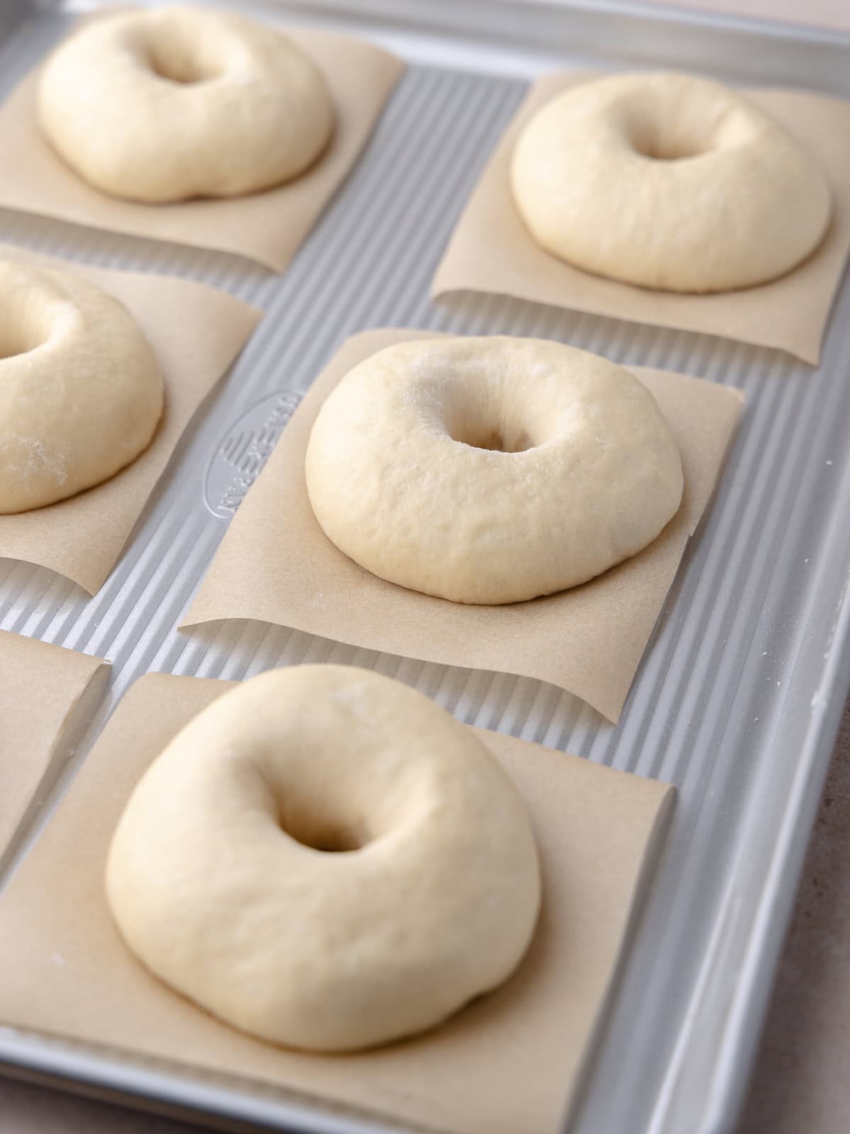 Shaped bagels are on a large baking tray.