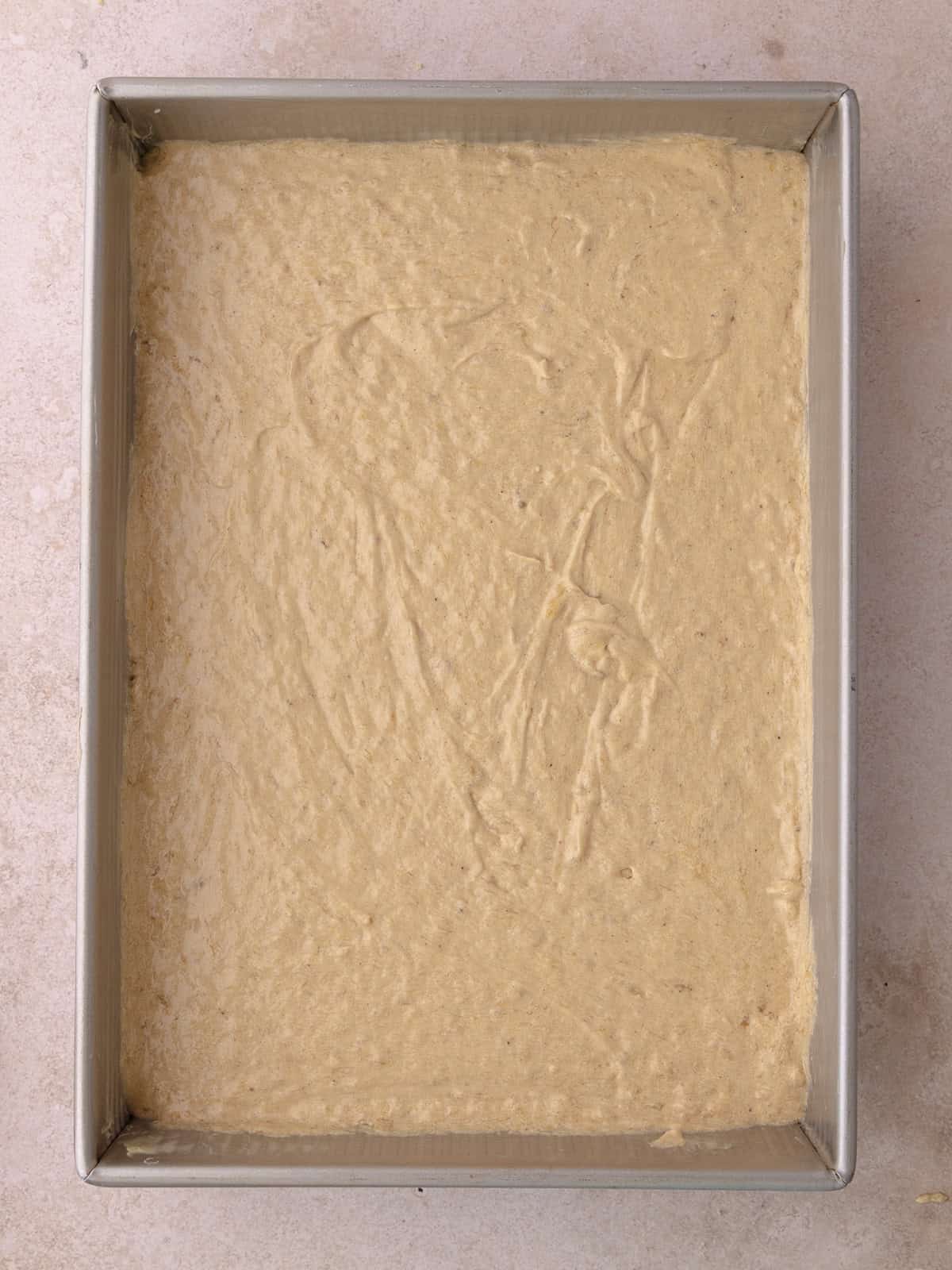 Spiced banana cake batter is poured into a buttered baking pan.