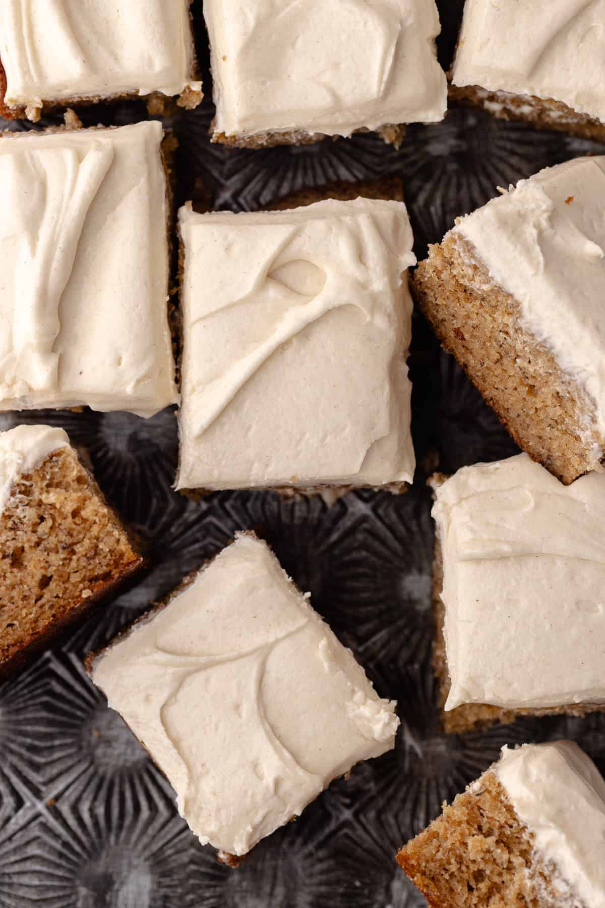 Spice banana cake frosted in cinnamon maple cream cheese frosting cut into squares sitting on a baking sheet.