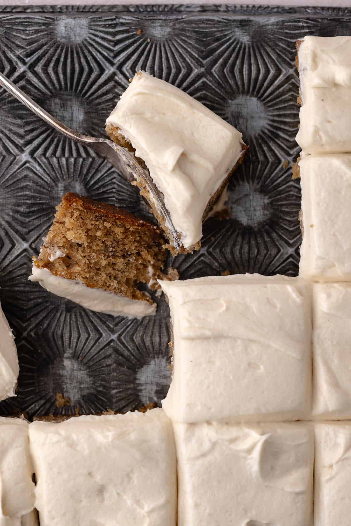 Spice banana cake frosted in cinnamon maple cream cheese frosting cut into squares sitting on a baking sheet.