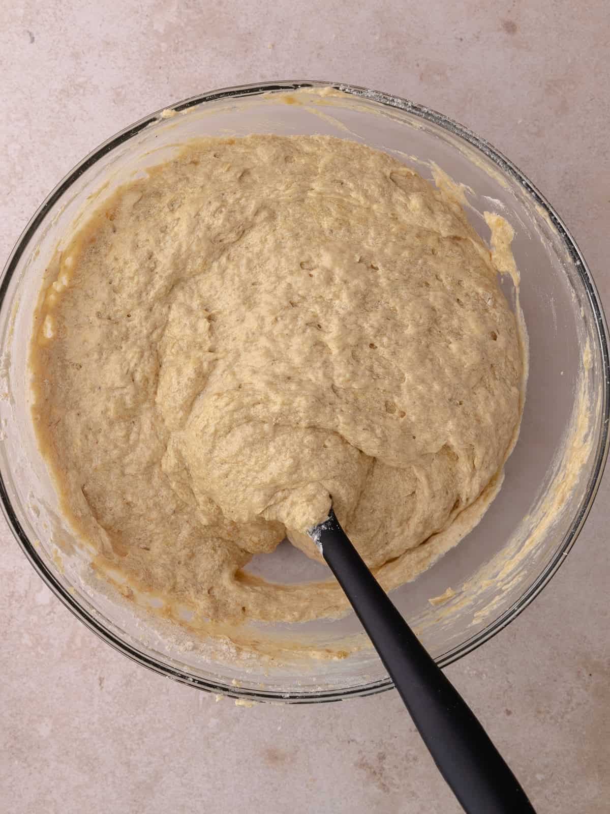 Flour is mixed into the batter. The batter is thick and sitting in a large glass mixing bowl.