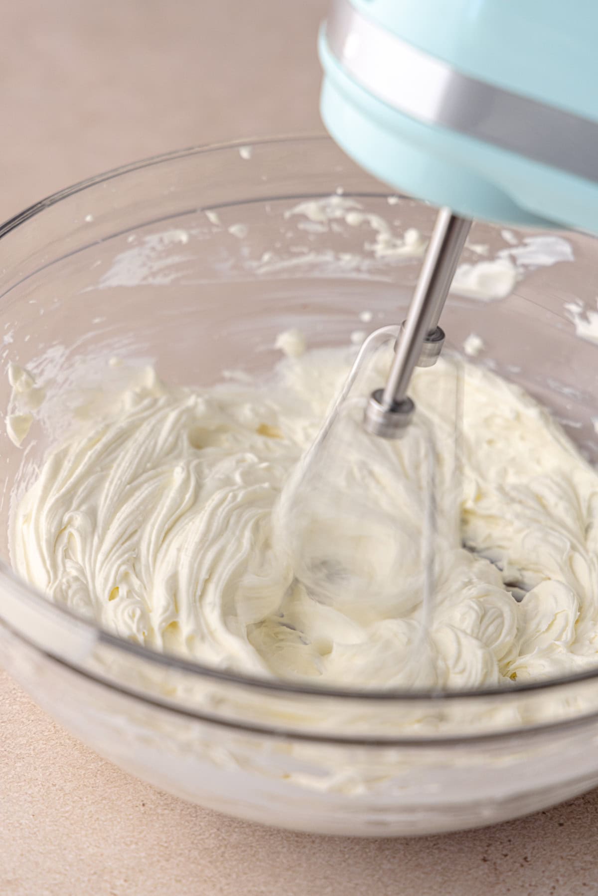 Bagel schmear, which is a spreadable cream cheese, is being whipped in a medium glass bowl.