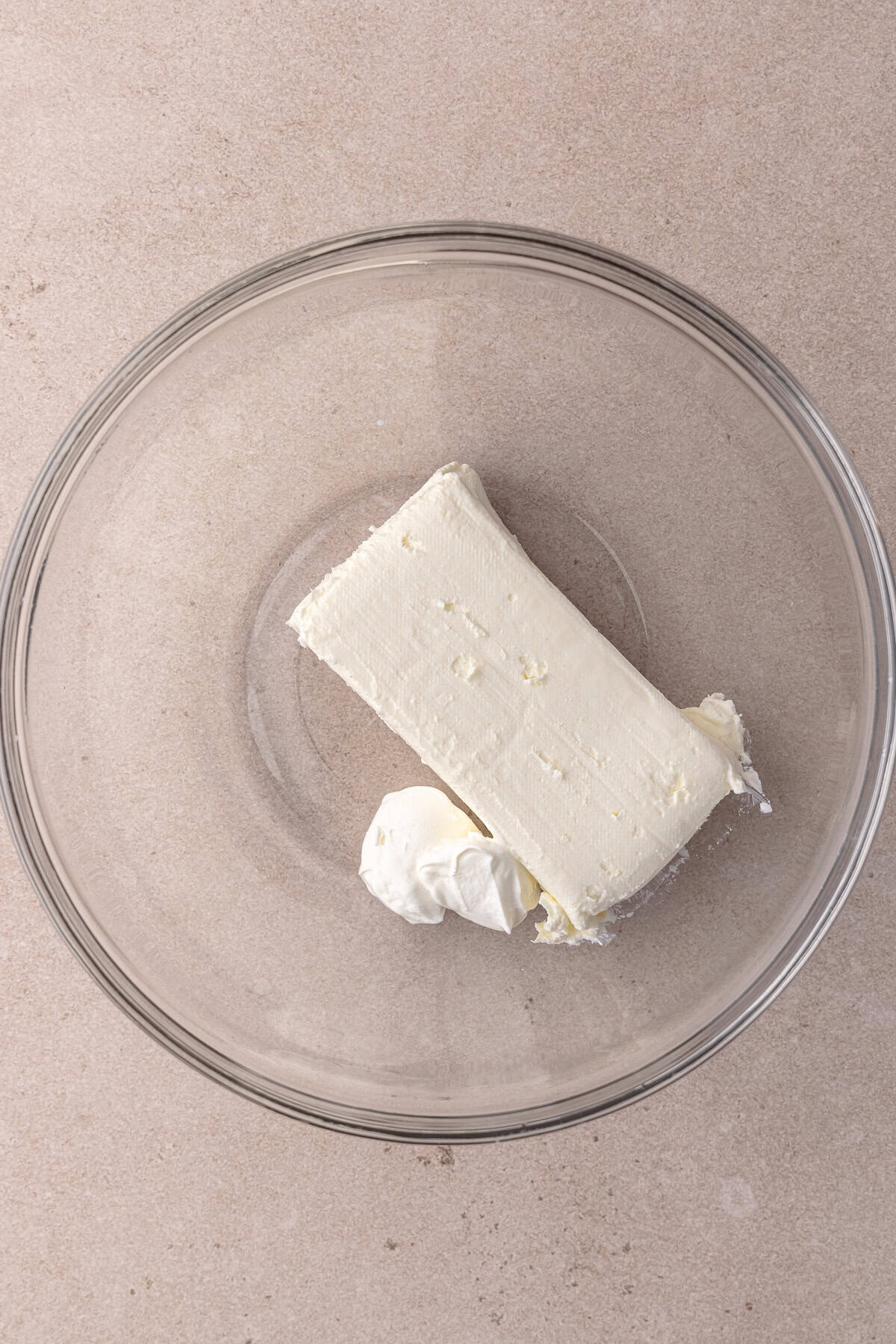 Cream cheese brick and Greek yogurt are sitting in a medium glass mixing bowl.