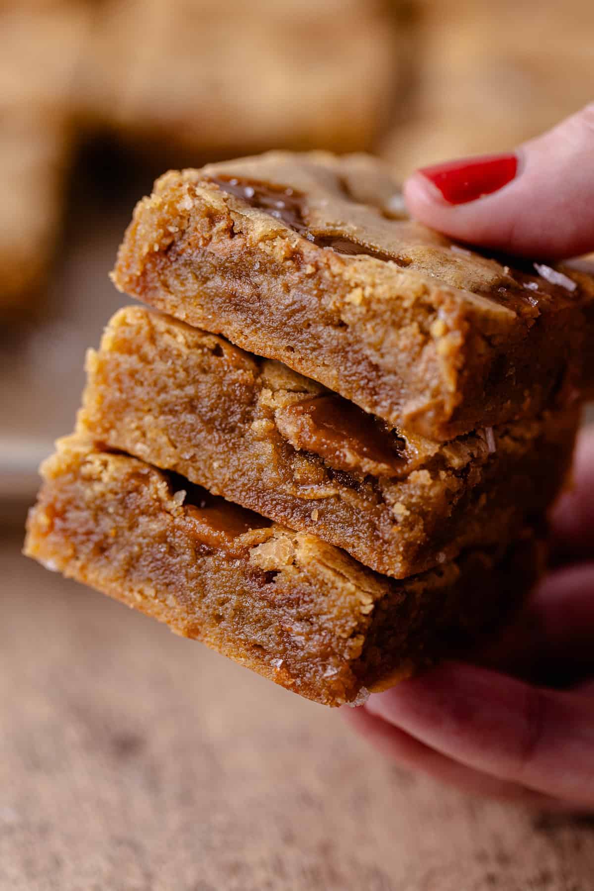 A hand holds a stack of three toffee cookie butter blondies.