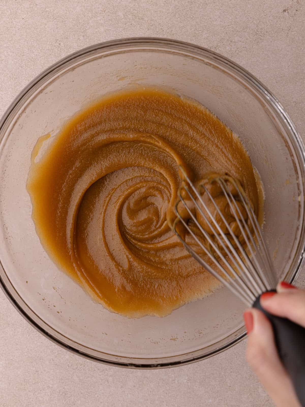 Melted butter and brown sugar are whisked together in a large glass mixing bowl.