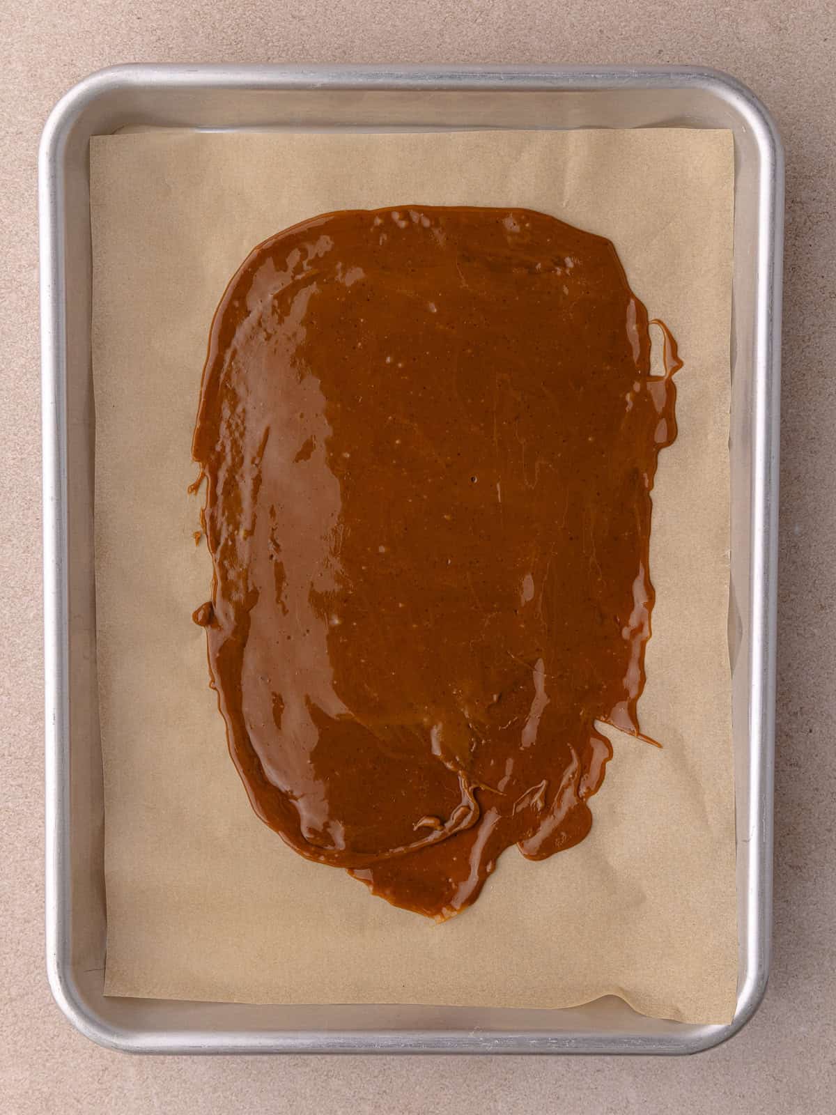 Toffee mixture is spread onto a small baking tray lined with parchment paper.